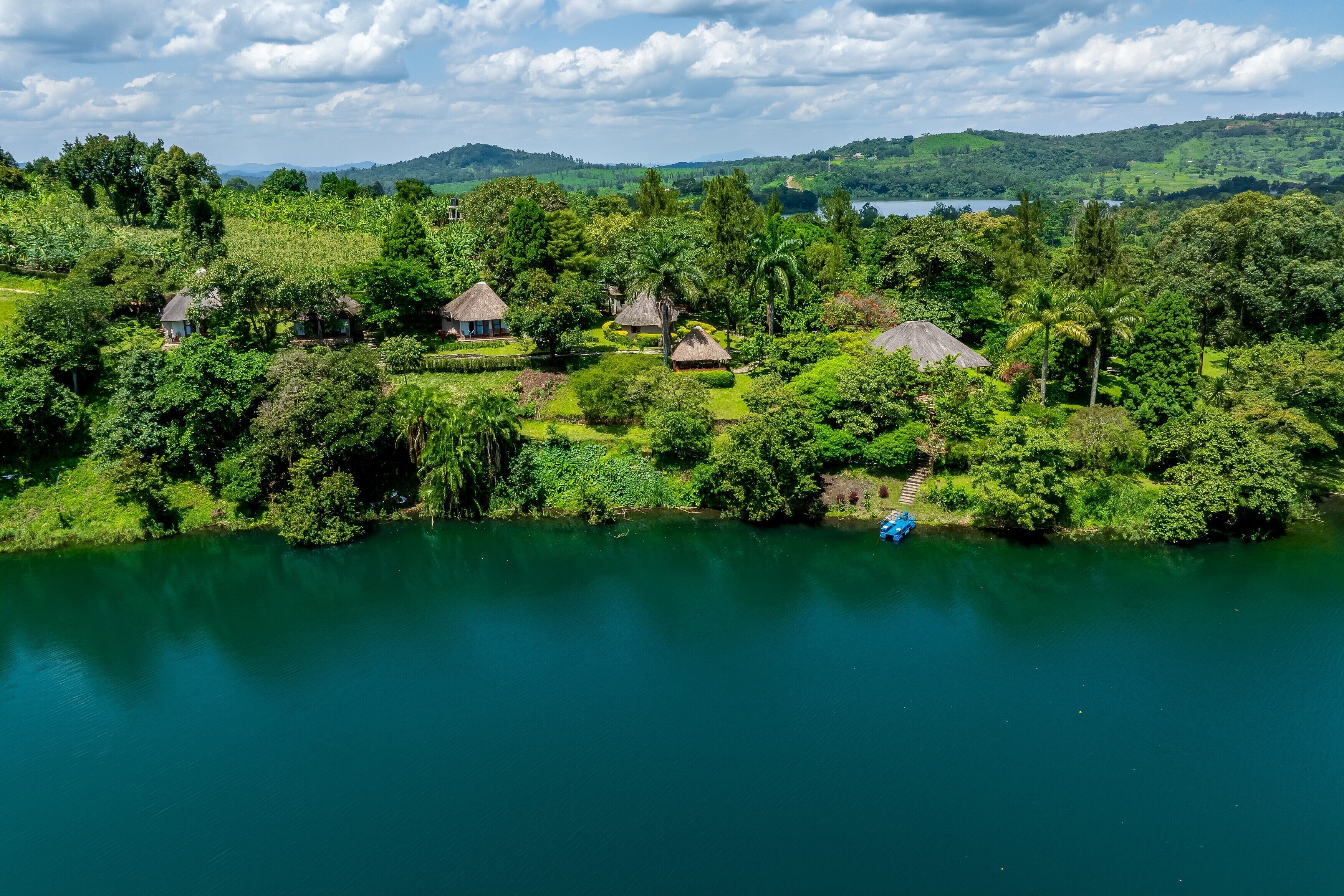 A lakeside property with multiple thatched-roof cottages surrounded by lush greenery and a clear view of the lake.