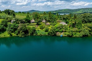 A lakeside property with multiple thatched-roof cottages surrounded by lush greenery and a clear view of the lake.