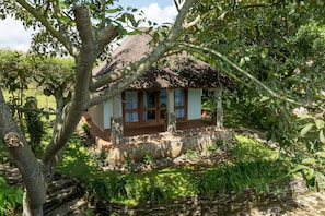 A house with a thatched roof, surrounded by lush greenery and a stone wall. - bahundu Safari Lodge (Fort Portal)
