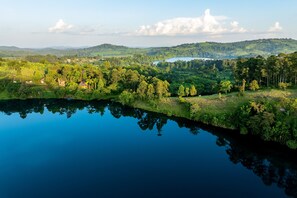 Un paisaje sereno con un lago tranquilo que refleja la vegetación circundante y colinas distantes.