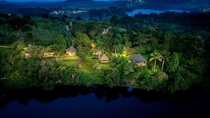 A secluded island with multiple thatched-roof cottages surrounded by dense greenery and a calm lake.