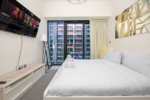 A hotel room with a large bed, a flat-screen TV mounted on the wall, a desk with a lamp, and a view of a building through the window. - Riviera 42 Studio · Lagoon Pool · Meydan (Dubai)