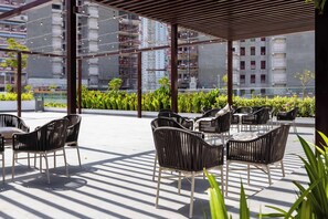 An outdoor seating area with wicker chairs and tables, surrounded by greenery and overlooking a cityscape. - Riviera 42 Studio · Lagoon Pool · Meydan (Dubai)