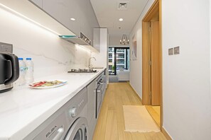 A modern kitchen with a built-in washing machine, a sink, and a countertop with water bottles and a plate. - Riviera 42 Studio · Lagoon Pool · Meydan (Dubai)