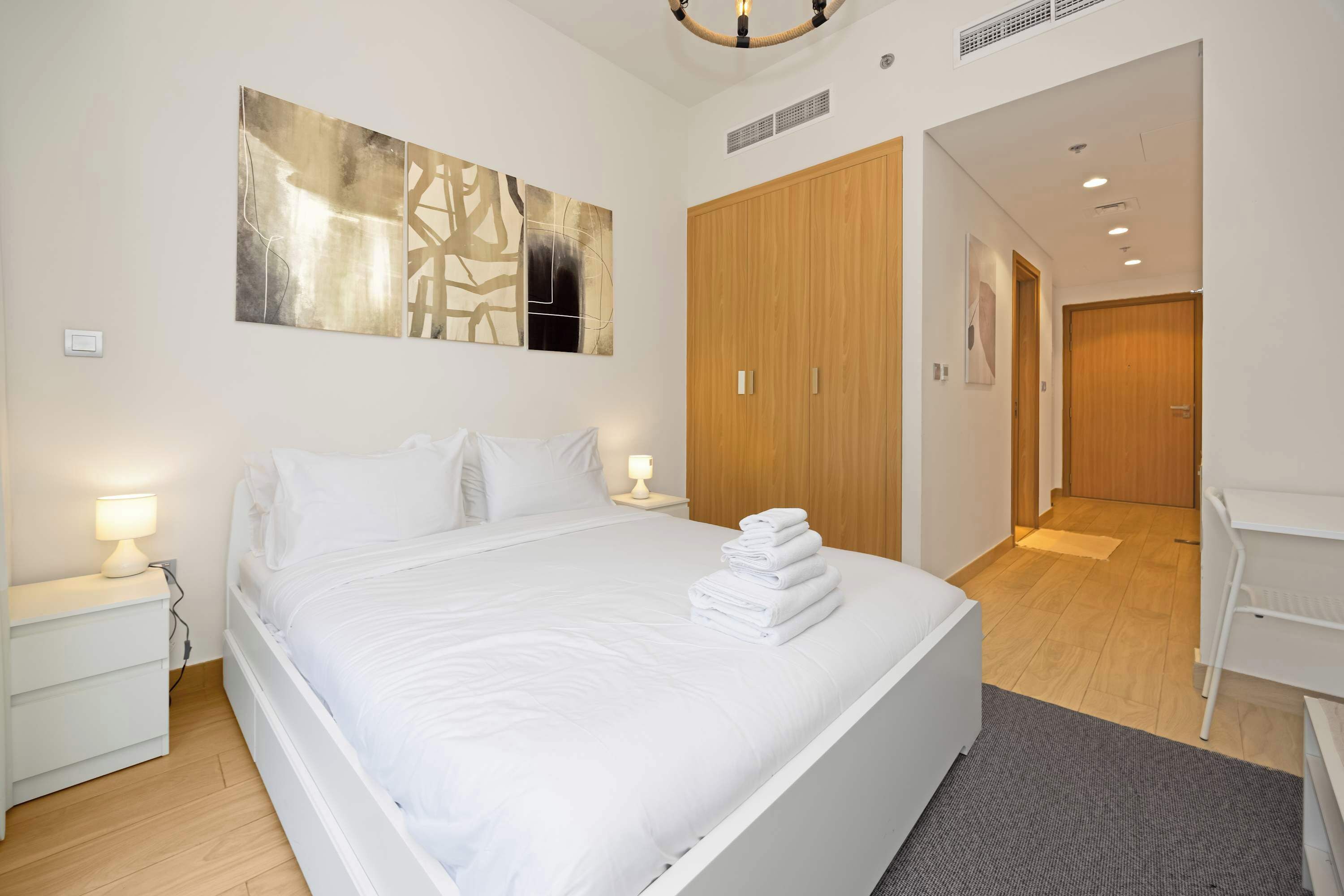 Une chambre à coucher moderne avec un grand lit, des lampes de chevet, une armoire en bois et un tableau au mur.