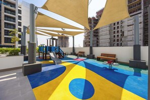 Un espace de jeux extérieur doté d’un sol coloré, de bancs et d’équipements de jeux.
