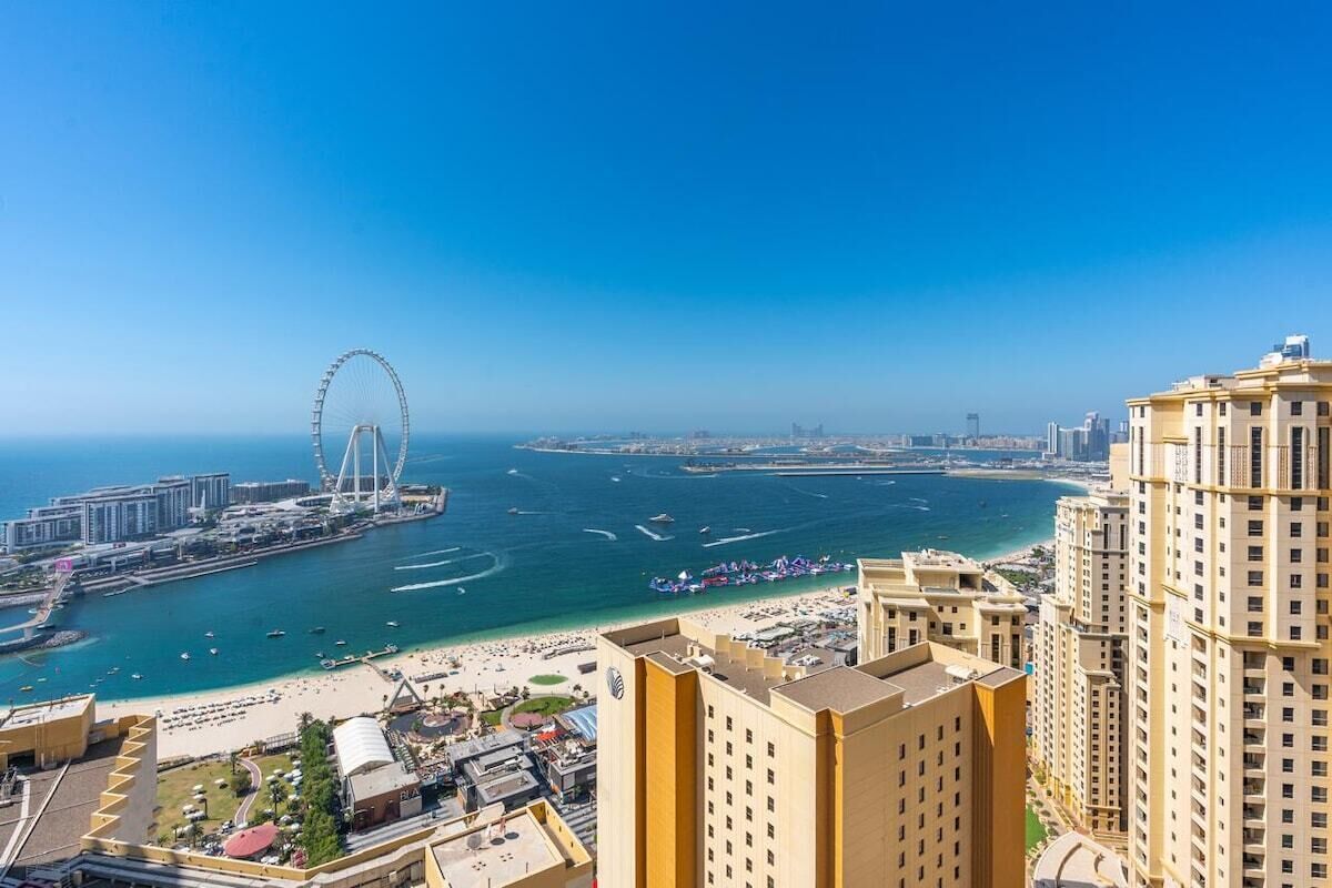 Un paisaje urbano costero con una noria destacada, edificios altos y una zona de playa.