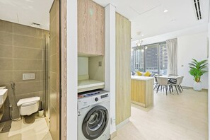 Een modern appartement met een kleine badkamer, een ingebouwde wasmachine, een eethoek met uitzicht en een woonruimte met een groot raam.