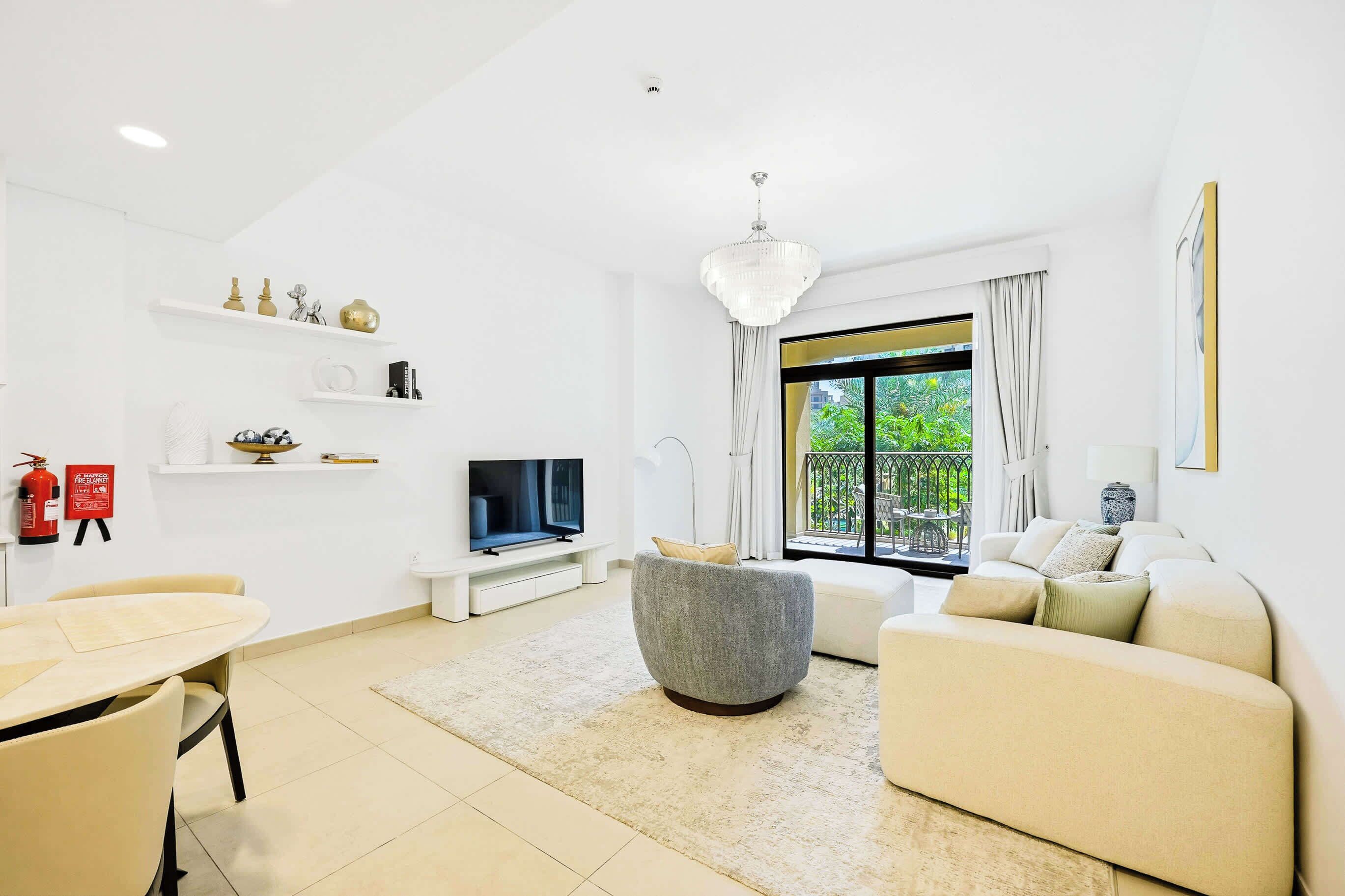 Un salon moderne avec un téléviseur à écran plat, un canapé gris, un canapé beige, une table à manger avec des chaises et un lustre.