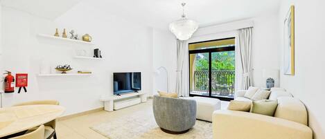 Un salon moderne avec un téléviseur à écran plat, un canapé gris, un canapé beige, une table à manger avec des chaises et un lustre.
