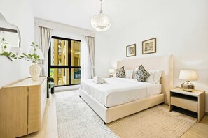 Ein modernes Hotelzimmer mit einem großen Bett, einem Schreibtisch, einem Sessel, einem Nachttisch, einer Lampe und Blick ins Freie.