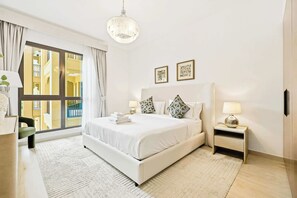 A hotel room with a large bed, a bedside table with a lamp, a window with curtains, and two framed pictures on the wall. - Madinat 1BR · Burj Al Arab View · Jumeirah (Dubai)