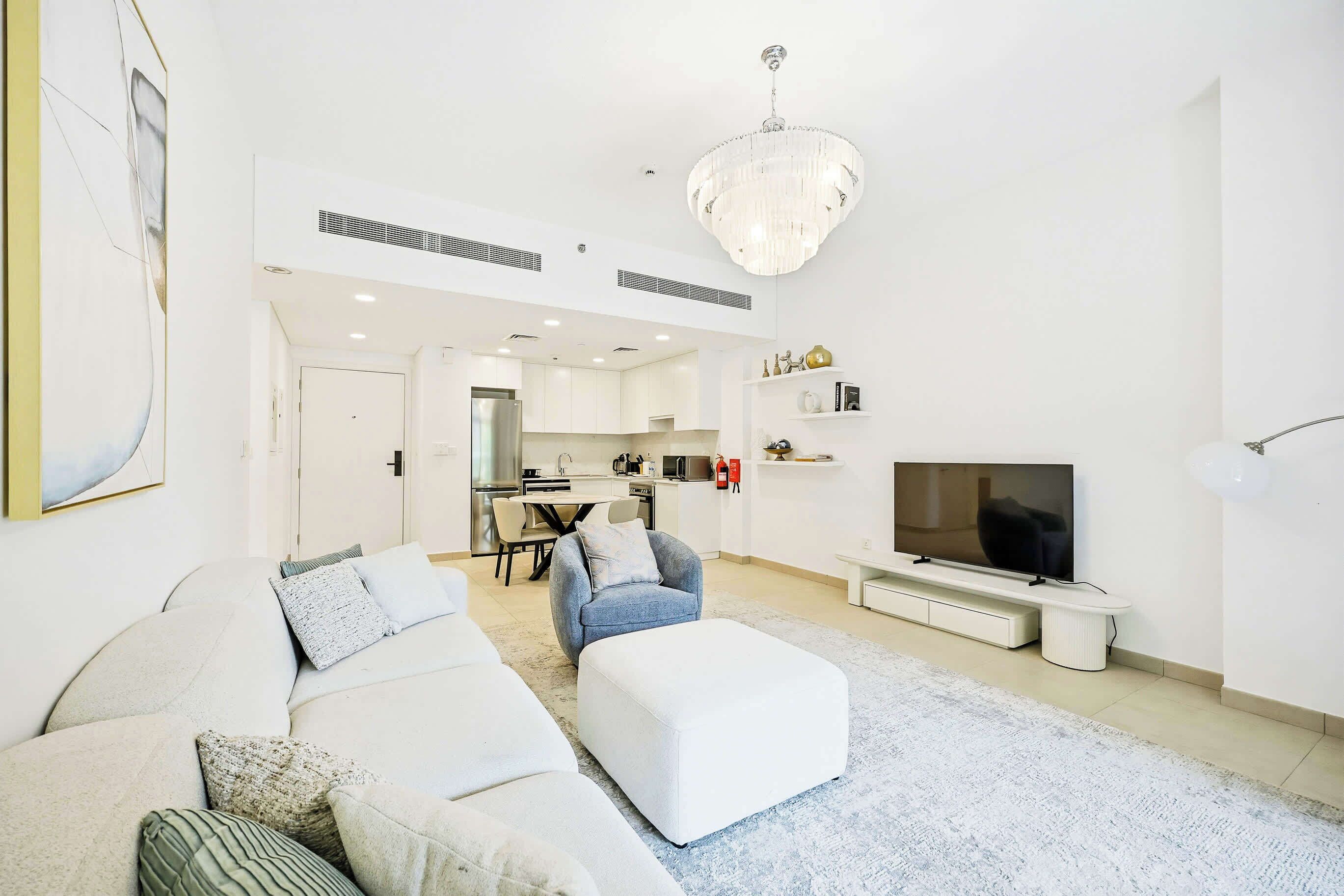 A modern living room with a white sofa, ottoman, and a flat-screen TV.