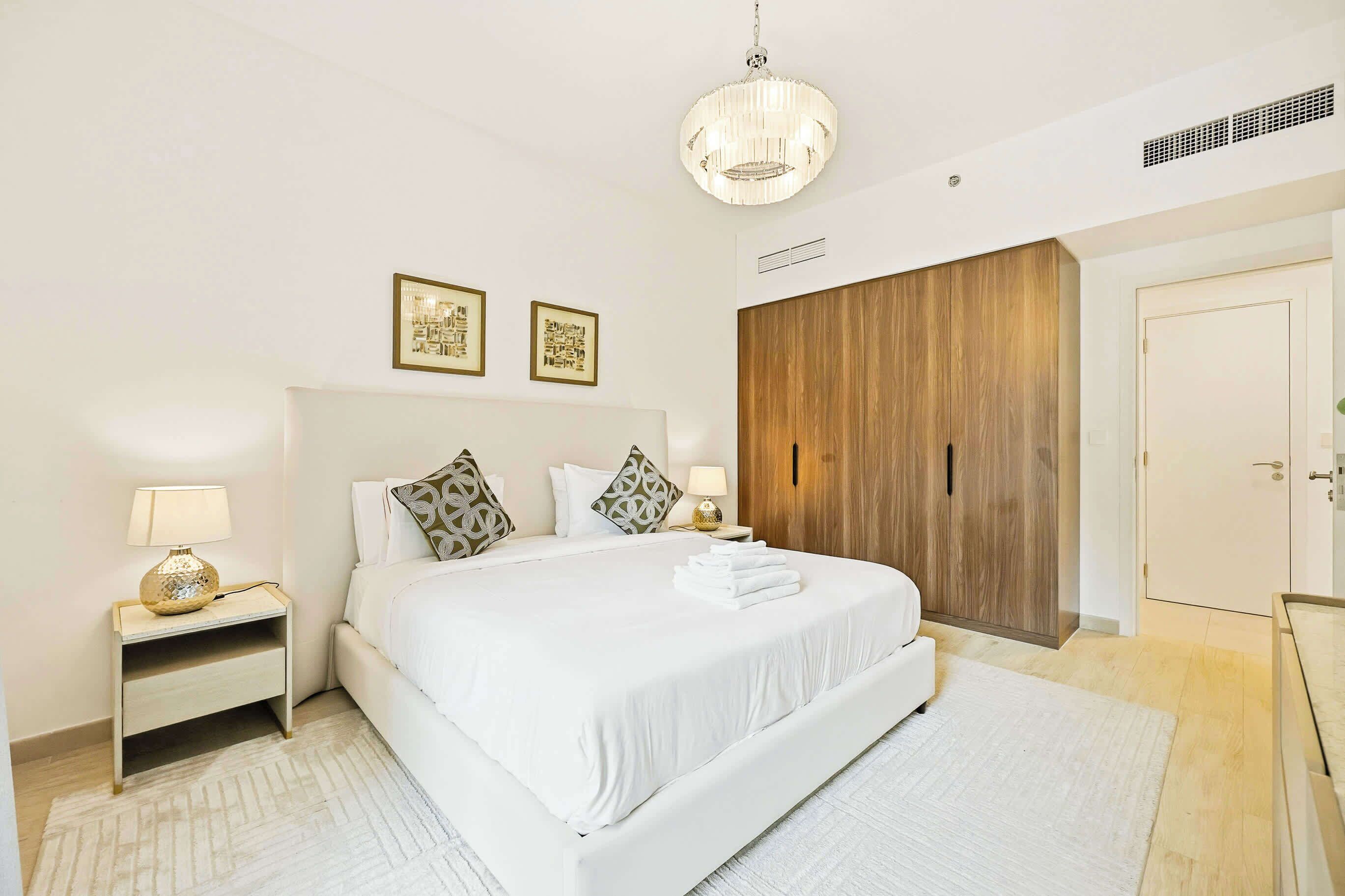 Une chambre d’hôtel avec un grand lit, des tables de chevet, une armoire en bois et un lustre.