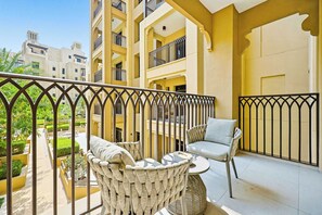 A balcony with wicker furniture, a small table, and a view of the surrounding buildings. - Madinat 1BR · Burj Al Arab View · Jumeirah (Dubai)