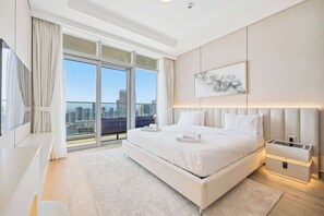 A modern hotel room with a large bed, a city view through floor-to-ceiling windows, a painting on the wall, and a bedside table with a lamp. - Imperial 3BR · Canal View · Downtown (Dubai)