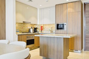 A modern kitchen with a central island, built-in oven, and a microwave. - Imperial 3BR · Canal View · Downtown (Dubai)