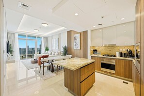 A modern kitchen with a central island, built-in oven, and a dining area with a sofa and chairs. - Imperial 3BR · Canal View · Downtown (Dubai)