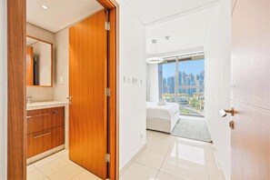 A hotel room with a wooden wardrobe, a bathroom with a mirror, and a city view through large windows. - Blvd Point 2BR · Burj View · Dubai Mall (Dubai)