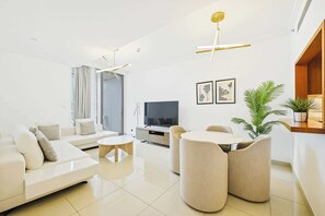 A modern living room with a sofa, coffee table, and chairs, a flat-screen TV, and a plant. - Blvd Point 2BR · Burj View · Dubai Mall (Dubai)