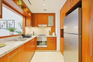 A modern kitchen with wooden cabinets, stainless steel appliances, and a built-in oven. - Blvd Point 2BR · Burj View · Dubai Mall (Dubai)