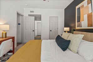 Een hotelkamer met een bed, bedlampen, een spiegel en een deur die naar een andere kamer leidt.