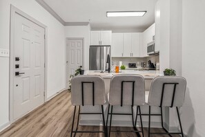Een moderne keuken met witte kasten, een roestvrijstalen koelkast en een bargedeelte met twee stoelen.