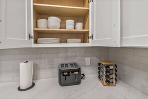 Een keuken met witte kastjes, een marmeren aanrechtblad, een broodrooster en een kruidenrek.