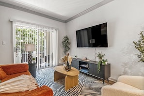 Een moderne woonkamer met een flatscreen televisie aan de muur, een bank, een salontafel en een kamerkleed met een patroon.