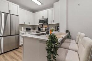 A modern kitchen with white cabinetry, stainless steel appliances, and a central island with seating. - Near NRG Stadium & DT| Pool & Gym, Free Parking (Houston)