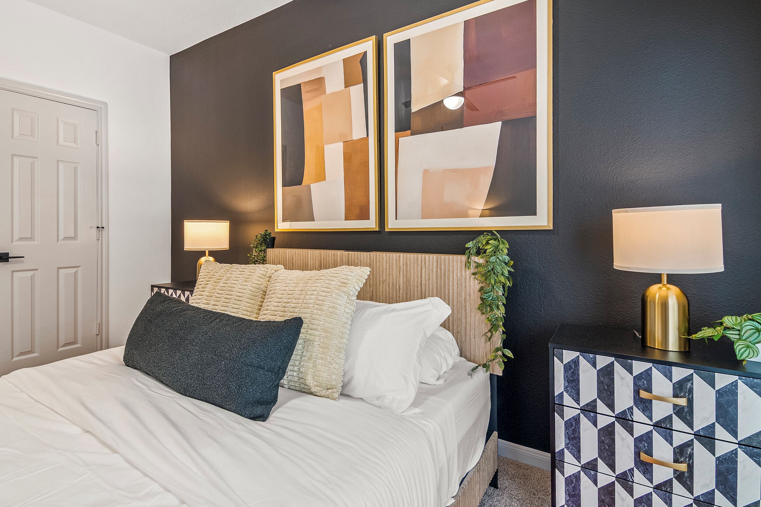 A bedroom with a bed, two bedside lamps, a decorative wall piece, and a geometric-patterned cabinet.