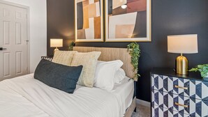 Une chambre à coucher comprenant un lit, deux lampes de chevet, un élément décoratif mural et un meuble aux motifs géométriques.
