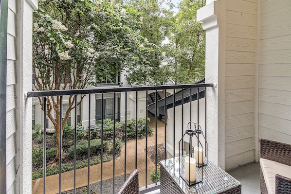 A balcony with a metal railing, a small table with a candle, and a view of a building with a staircase.