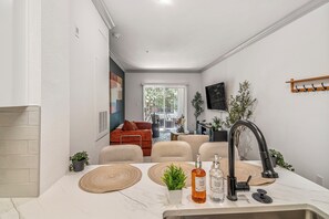 A compact kitchen with a modern faucet, a sink, and a countertop. There is a window with blinds, a small plant, and a wall-mounted TV.