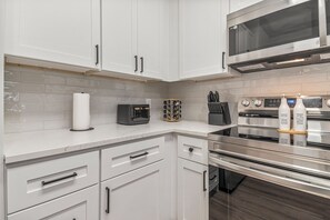 A modern kitchen with white cabinets, stainless steel appliances, and a marble countertop.