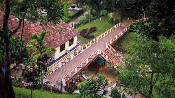 Un edificio de dos pisos con tejado de tejas rojas, un puente de madera y un jardín bien cuidado.