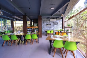 Een restaurant met meerdere tafels en stoelen, grote ramen en een behang met patroon.