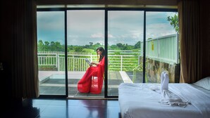 Habitación de hotel con un amplio ventanal corredero que da a un balcón con vistas a un paisaje verde y una cerca blanca.