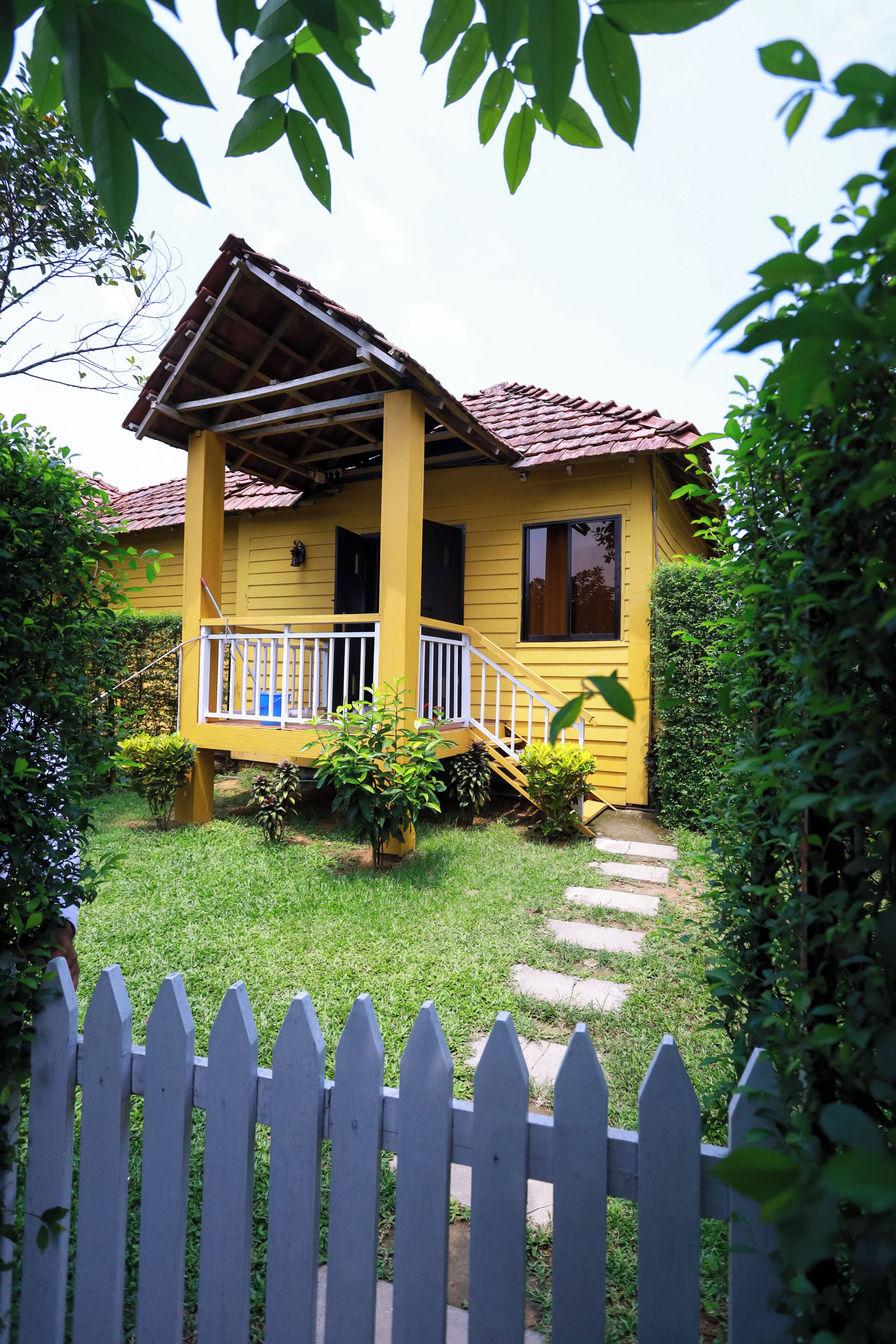 A yellow house with a porch, surrounded by greenery.