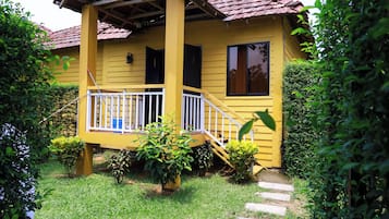 A yellow house with a porch, surrounded by greenery.