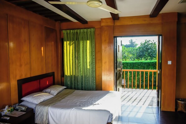A hotel room with a bed, bedside table, and a view of a balcony with a railing.