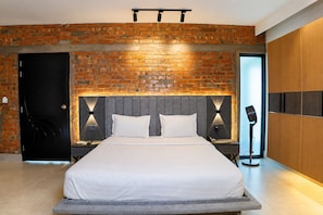 A modern bedroom with a brick wall, a bed with white linens, and a nightstand with a lamp.