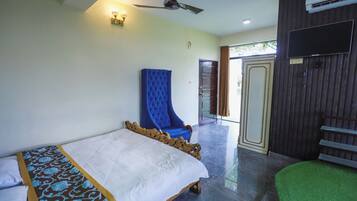 A hotel room with a bed, a blue armchair, a ceiling fan, and a TV mounted on the wall.