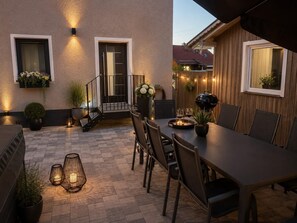 En uteplats med ett bord dukat för måltider, omgiven av stolar, och en grill.