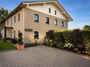En modern byggnad med ett platt tak, flera fönster och ett stenbelagt entréområde med planterade blommor i krukor.