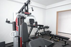 Een sportschool met een halterbank, gewichten en een kabelapparaat.
