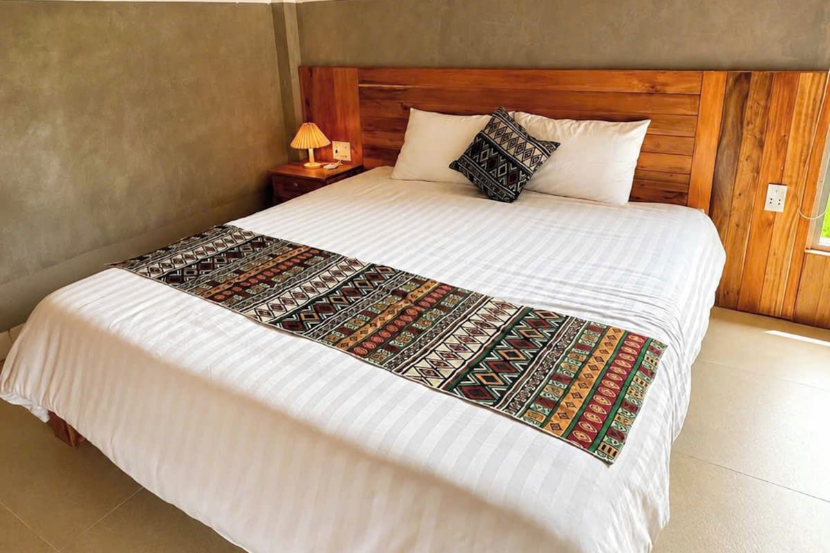 A bed with a wooden headboard, a patterned bedspread, and a bedside table with a lamp.