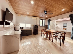 A modern kitchen with a built-in microwave, a refrigerator, and a dining area with a wooden table and chairs. - The Aurora Retreat (Phu Quoc)