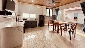 A modern kitchen with a built-in microwave, a refrigerator, and a dining area with a wooden table and chairs. - The Aurora Retreat (Phu Quoc)