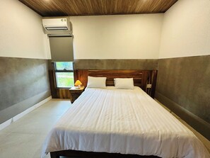 A bedroom with a bed, a nightstand, a lamp, and an air conditioning unit. - The Aurora Retreat (Phu Quoc)